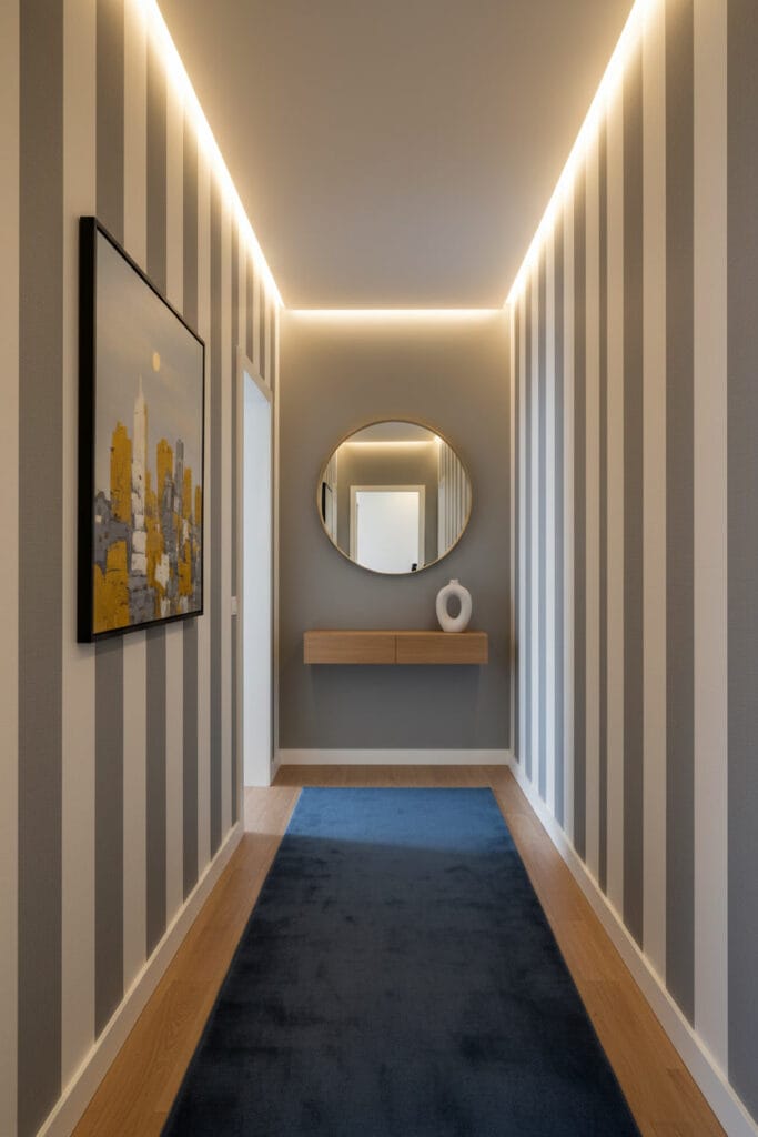 Couloir deco avec papier peint rayures verticales gris et crème, miroir laiton, console chêne, tableau abstrait urbain et éclairage doux.
